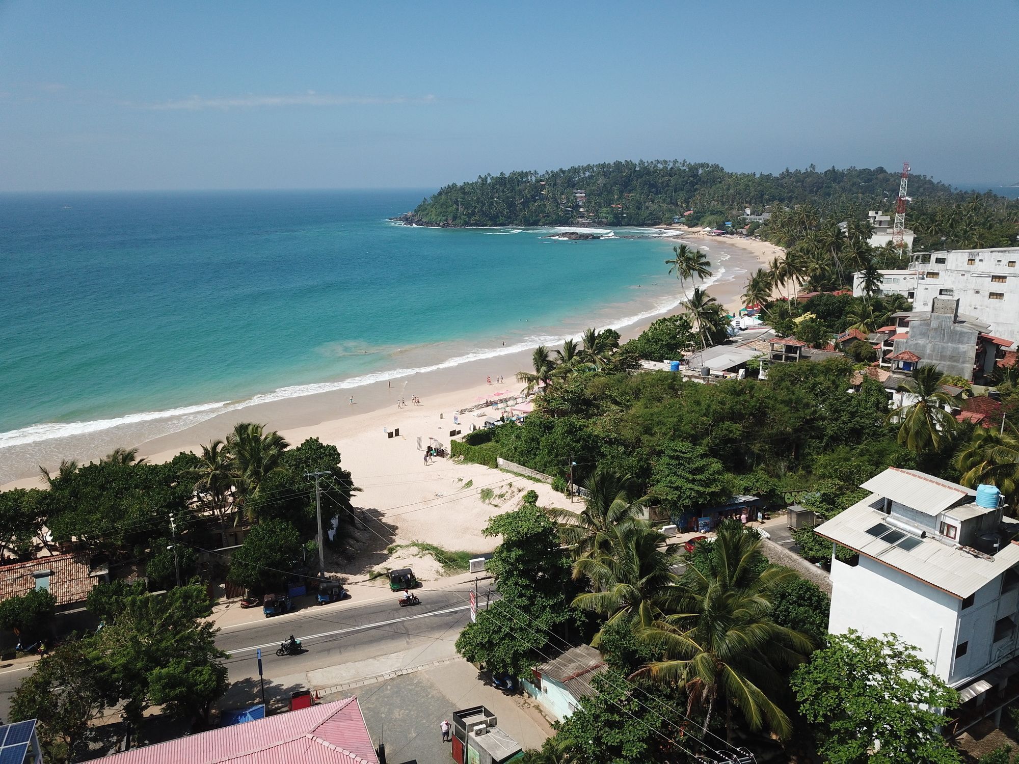 A coastal area with a beach, buildings, and a road.