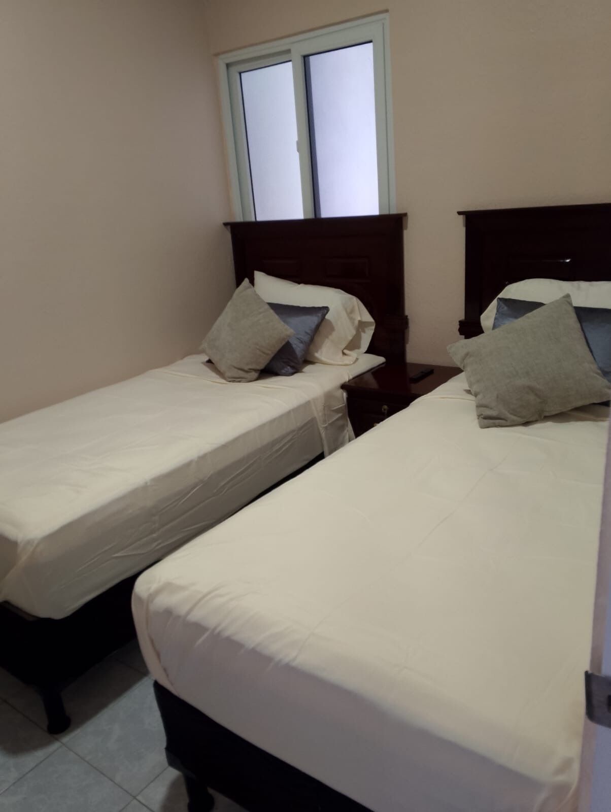 Une chambre avec deux lits simples, une fenêtre et une table de chevet avec une lampe.