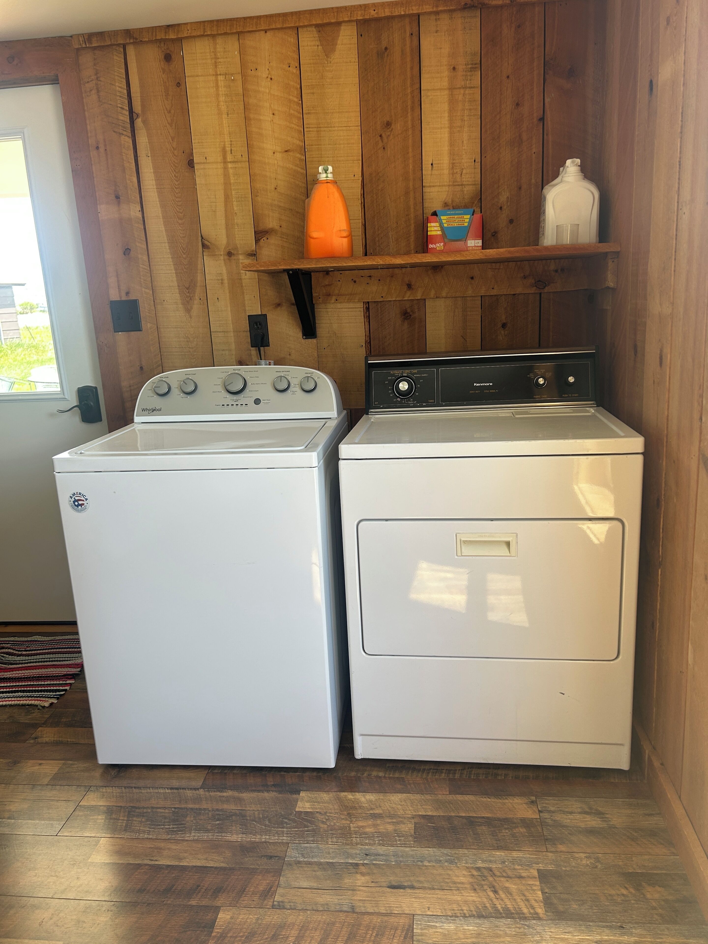 Un espace buanderie équipé d’un lave-linge Whirlpool et d’un sèche-linge Kenmore, avec des murs en bois et une étagère sur laquelle se trouvent une bouteille et une boîte.
