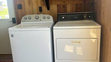 Un espace buanderie équipé d’un lave-linge Whirlpool et d’un sèche-linge Kenmore, avec des murs en bois et une étagère sur laquelle se trouvent une bouteille et une boîte.