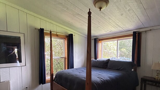 A four-poster bed in a room with wooden floors, a radiator, and a window with curtains.