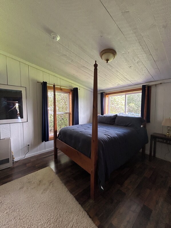 A four-poster bed in a room with wooden floors, a radiator, and a window with curtains.