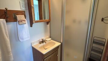 Un baño con tocador de madera, lavamanos, espejo, toallero y zona de ducha.