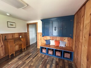 A wooden-floored hallway with a bench, blue cabinets, and a door leading to another room.