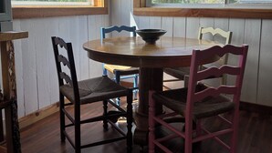 A dining area with a round table, four chairs, and two windows with a view of trees.