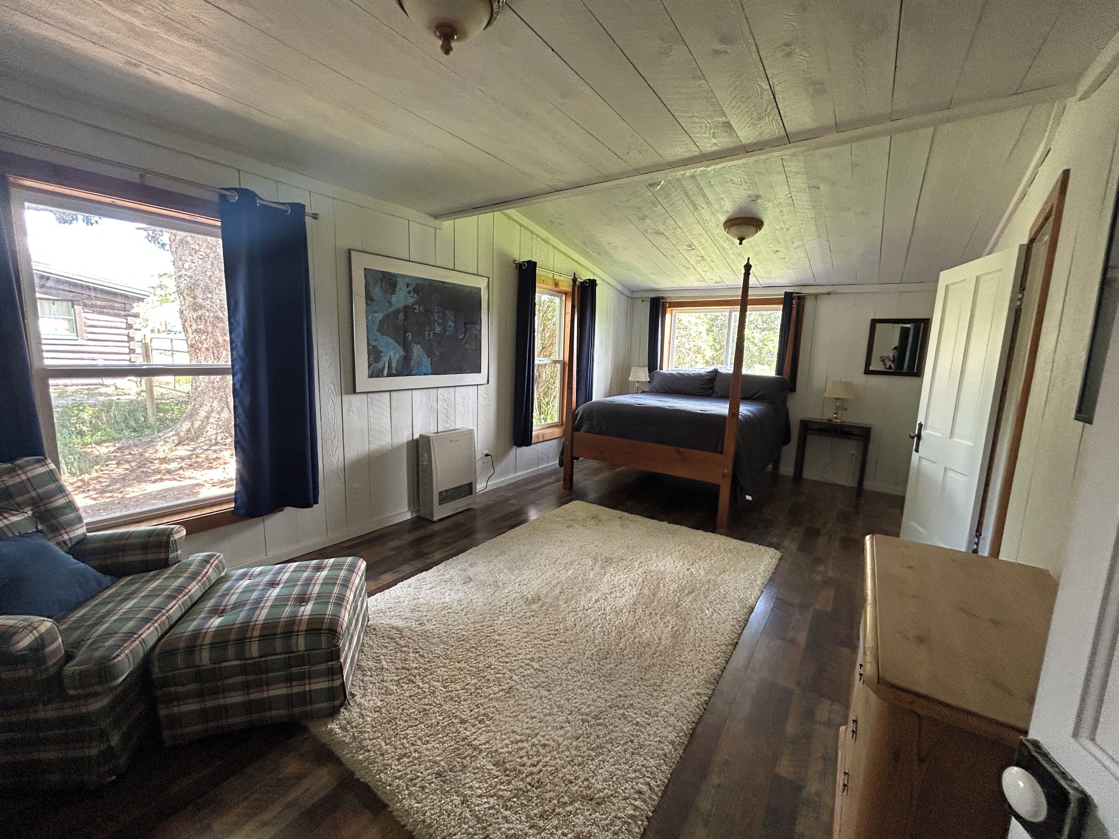 A bedroom with a bed, a window, a painting, and a heater.