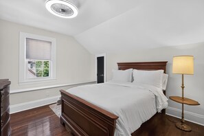 A bedroom with a bed, a bedside table, a lamp, a window with blinds, and a door.