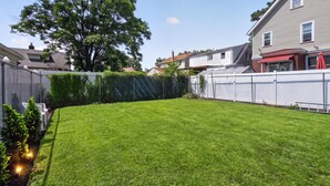 Ein gepflegter Garten mit einem ordentlich geschnittenen Rasen, einem großen Baum und einem weißen Zaun.