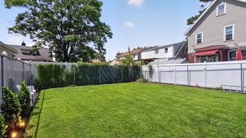 Un jardin bien entretenu, avec une pelouse soigneusement taillée, un grand arbre et une clôture blanche.