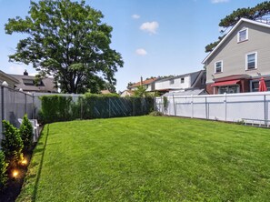 A well-maintained backyard with a neatly trimmed lawn, a large tree, and a white fence. - Historic Forest Hill Single Family Near NYC (Newark)