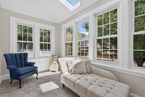 A room with a large window, a blue armchair, a beige sofa, and a small wooden nightstand. - Historic Forest Hill Single Family Near NYC (Newark)