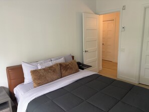 A bedroom with a bed, pillows, a nightstand, and a door leading to another room. - Le Diamant Bleu in Quebec City ~GYM~GARAGE~Downtown (Québec)