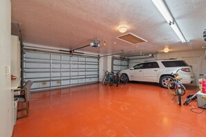 A garage with a red floor, a white SUV, and several bicycles. - Peaceful, Canal Front Home w/ Heated Pool - Surfside Beach House (Apollo Beach)