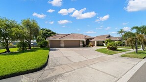 A residential property with a driveway leading to a garage, surrounded by well-maintained lawns and trees. - Peaceful, Canal Front Home w/ Heated Pool - Surfside Beach House (Apollo Beach)