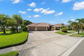 A residential property with a driveway leading to a garage, surrounded by well-maintained lawns and trees. - Peaceful, Canal Front Home w/ Heated Pool - Surfside Beach House (Apollo Beach)