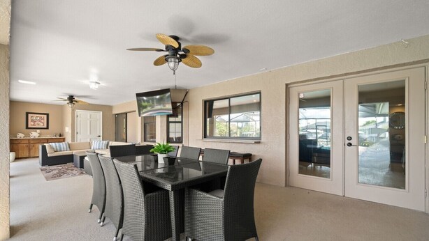 A dining area with a table and chairs, a ceiling fan, and a television mounted on the wall. - Peaceful, Canal Front Home w/ Heated Pool - Surfside Beach House (Apollo Beach)