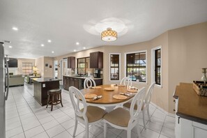A spacious kitchen with a dining area, white chairs, and a central island. - Peaceful, Canal Front Home w/ Heated Pool - Surfside Beach House (Apollo Beach)