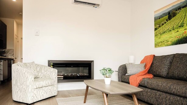Uma sala de estar com sofá, poltrona, mesa de centro, lareira e um quadro na parede.