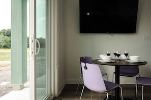 A dining area with a table set for four, a flat-screen TV mounted on the wall, and a sliding glass door leading to an outdoor area. - New Vineyard Cottage in Niagara Wine Country | 2BR | Pet Friendly (Lincoln)