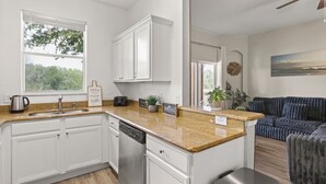 A modern kitchen with white cabinetry, granite countertops, and a dishwasher. There is a window providing natural light and a view of trees. - 4 BD/ 3 BA/ Regal Palms (3214 CA) (Davenport)