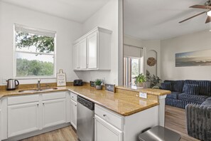 Una cocina moderna con armarios blancos, encimeras de granito y lavavajillas. Hay una ventana que proporciona luz natural y vistas a árboles.