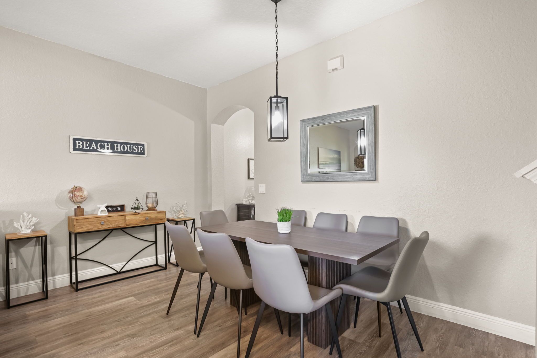 Un comedor con una mesa larga, seis sillas, una mesita de madera, un globo terráqueo y un cartel que dice 'BEACH HOUSE'.