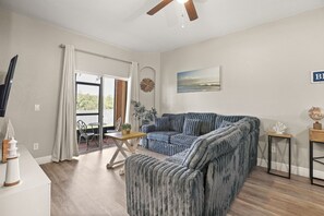 Una sala de estar con sofá, mesa de comedor y vistas al exterior a través de un ventanal.