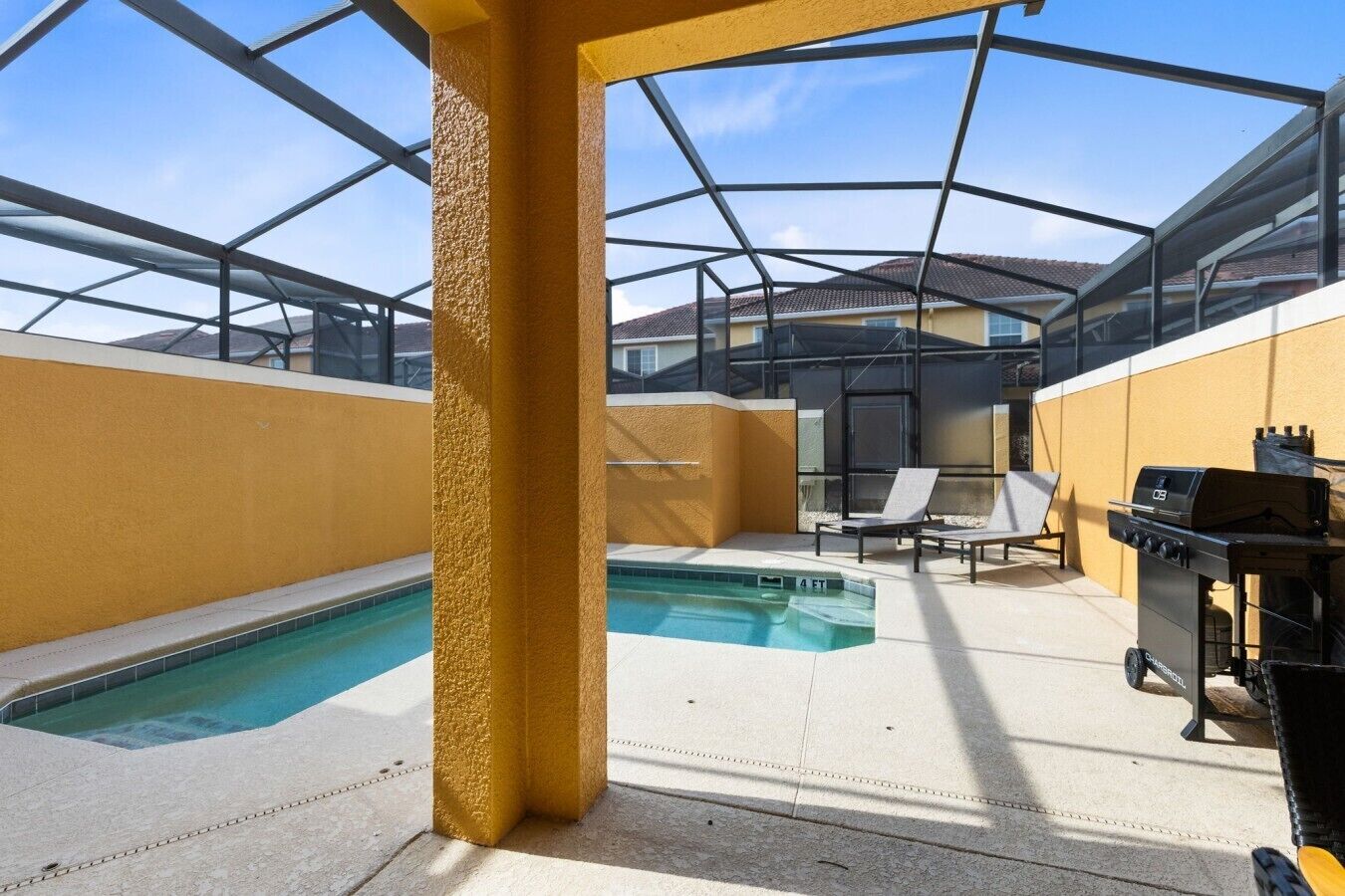 Un espace extérieur abrité comprenant une piscine, des chaises longues et un barbecue.