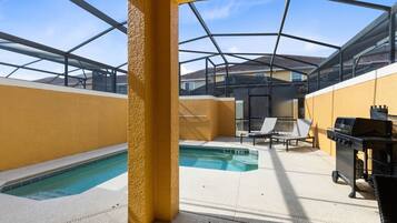 Un espace extérieur abrité comprenant une piscine, des chaises longues et un barbecue.