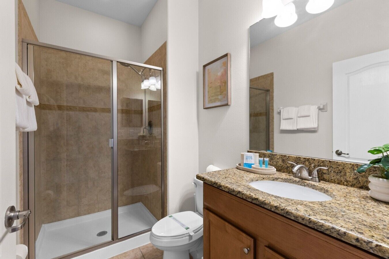Une salle de bain dotée d’une douche à parois de verre, d’un lavabo avec un plan de travail en granit et d’un miroir au-dessus du lavabo.