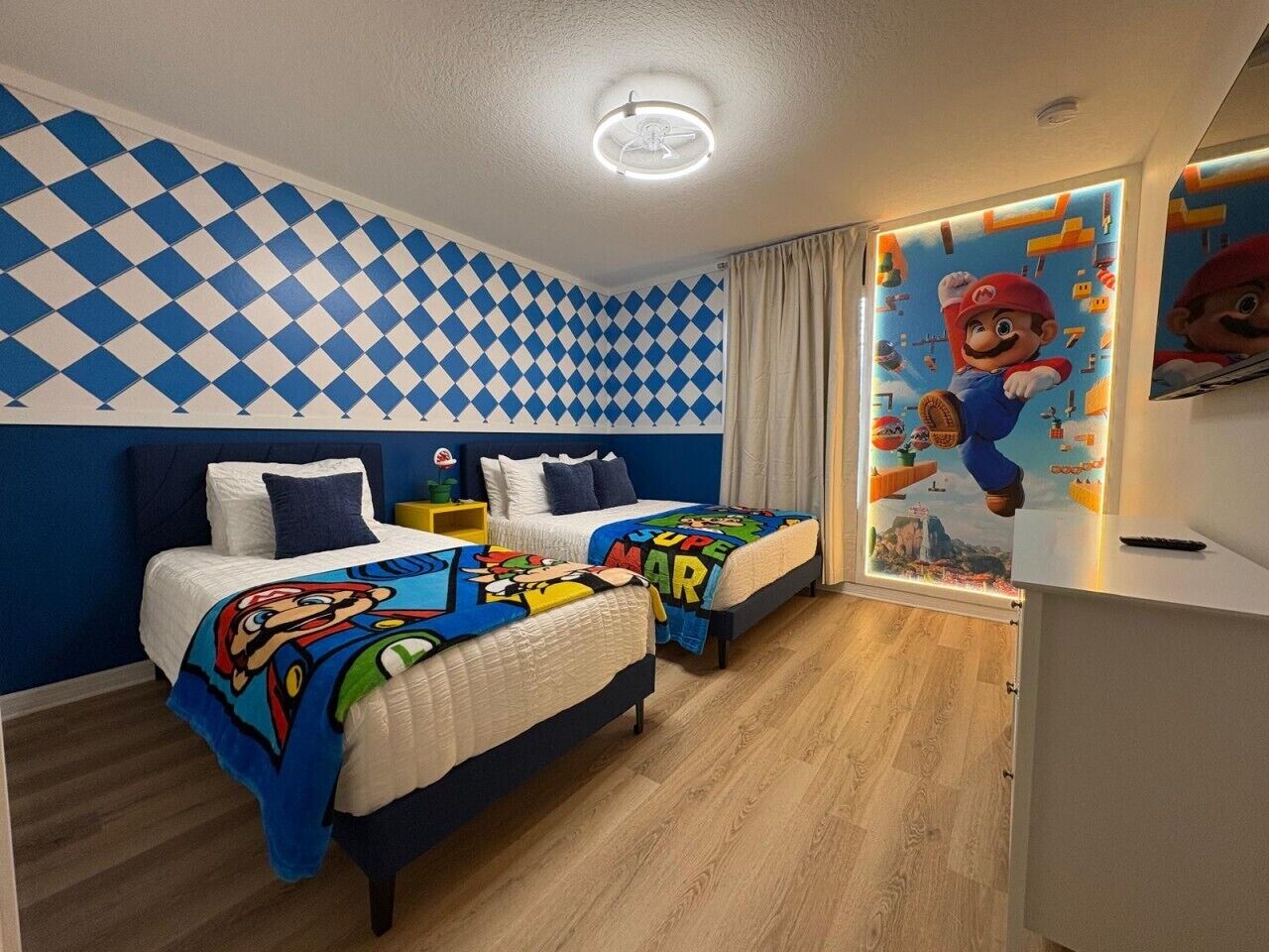 Un dormitori amb dos llits, un ventilador de sostre i un mural amb tema de Mario.