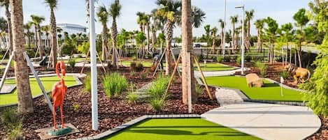 A well-maintained golf course with manicured grass, palm trees, and a sculpture of a flamingo.