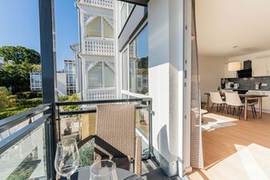 Ein Balkon mit Glastrennwand, ein Tisch mit Gläsern und Blick auf ein Gebäude mit weißen Balkonen.