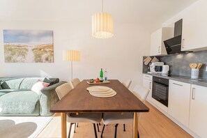 A modern kitchen with a dining table, chairs, and a sofa in the living area. - Ostseeglück Sassnitz - Stylish Apartment by the Sea (Sassnitz)