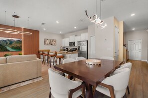A modern kitchen with white cabinets, a stainless steel refrigerator, and a dining area with a wooden table and white chairs. - 4 BD/ 3 BA/ Storey Lake (4796 CT) (Kissimmee)
