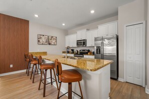 A modern kitchen with white cabinets, stainless steel appliances, a granite countertop, and bar stools. - 4 BD/ 3 BA/ Storey Lake (4796 CT) (Kissimmee)