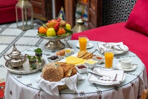 Un desayuno con frutero, pan, huevos y jugo sobre una mesa.