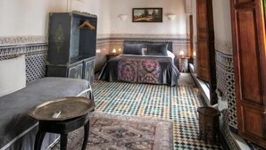 Une pièce avec un sol à motifs, un lit recouvert d’une couvre-lit à motifs, une petite table et un plafond décoratif.