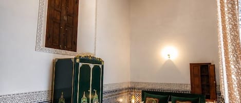 A room with a patterned floor, a bed with green bedding, a wooden wardrobe, and a chandelier.