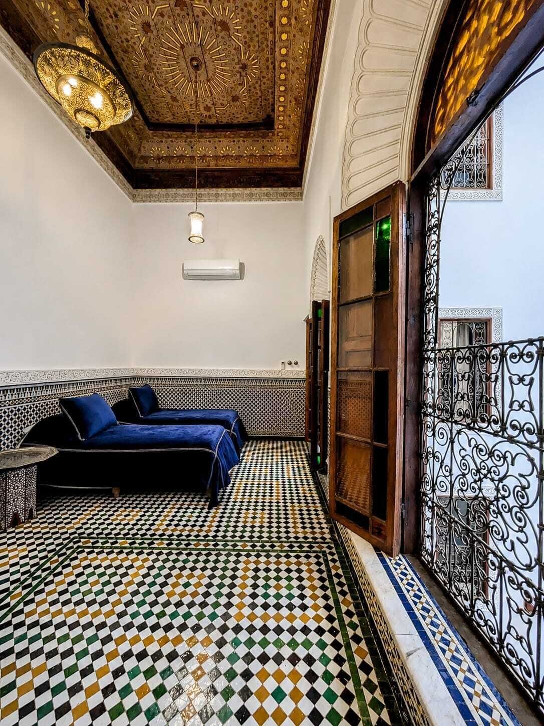A room with a checkered floor, two beds, a hanging light fixture, and a decorative ceiling.