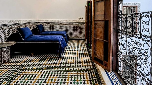 Une pièce avec un sol à carreaux, deux lits, un luminaire suspendu et un plafond décoratif.