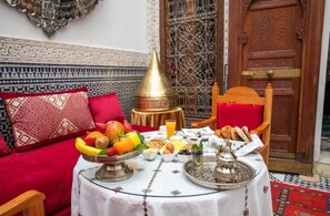 A traditional Moroccan breakfast setting with a table set for two, featuring a variety of fruits, bread, and a teapot. - Riad Arabella  (Fes)