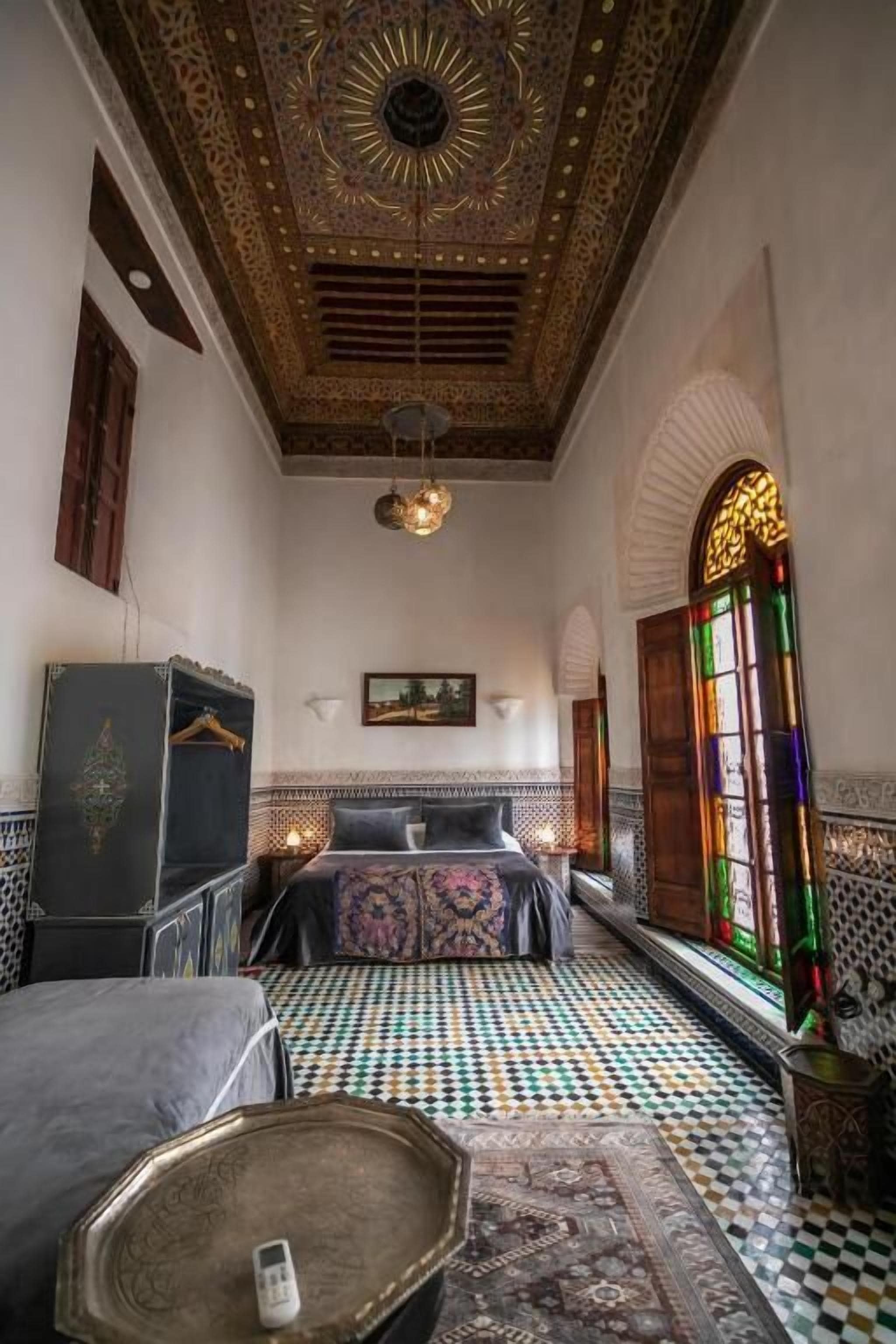 A room with a patterned floor, a bed with a headboard, a hanging light fixture, and a decorative ceiling.