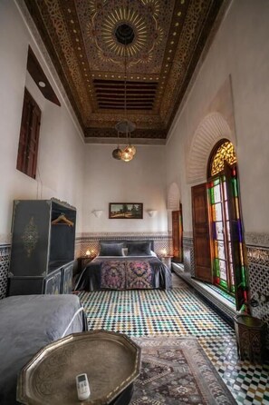 Una habitación con piso estampado, una cama con cabecera, una lámpara colgante y techo decorativo.