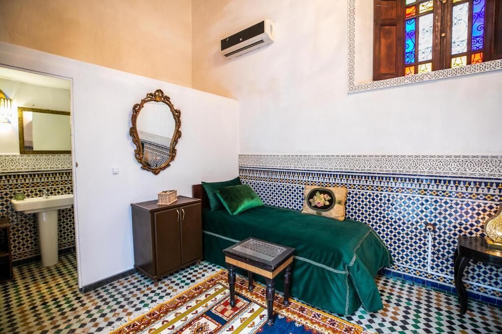 A room with a patterned floor, a green sofa, a small table, a cabinet, and a mirror on the wall.