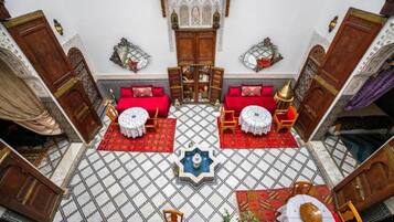 Ein Zimmer mit kariertem Boden, zwei roten Sofas, einer zentralen Fontäne und traditioneller Einrichtung.