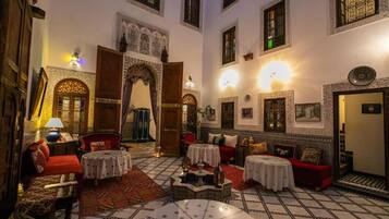 Un interior tradicional marroquí con arcos ornamentados, suelos de azulejos y una variedad de opciones de asiento, incluyendo sofás y mesas.