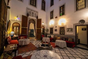Un interior tradicional marroquí con arcos ornamentados, suelos de azulejos y una variedad de opciones de asiento, incluyendo sofás y mesas.