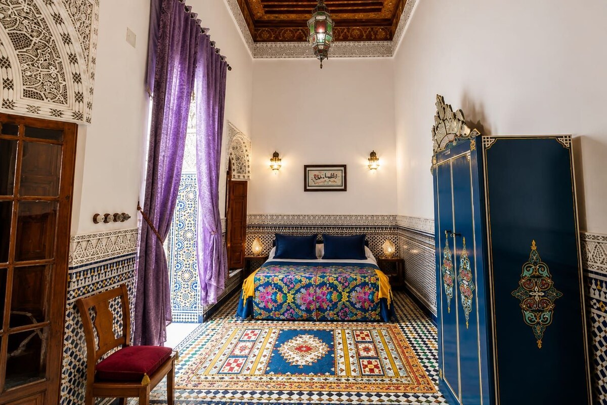 Una habitación con piso estampado, una cama con colcha colorida, un armario de madera y un adorno decorativo en la pared.
