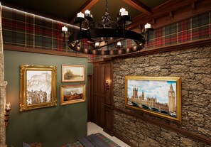 Une pièce avec un mur en pierre, des poutres en bois et un lustre orné de bougies. Des tableaux encadrés sont accrochés au mur.